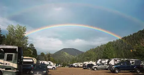 A double rainbow arches over a campground surrounded by mountains and trees.