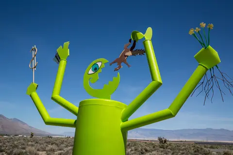 A brightly painted green sculpture stands outdoors against a clear blue sky.