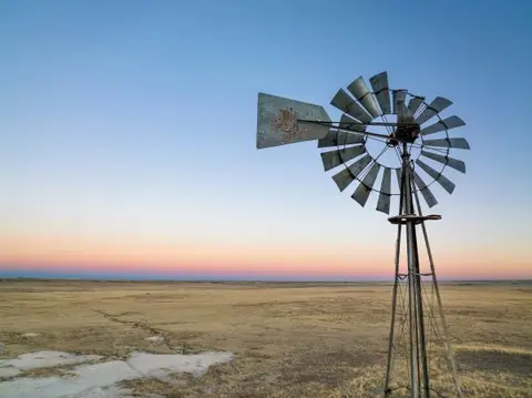 A rustic windmill stands in a dry field at sunset.