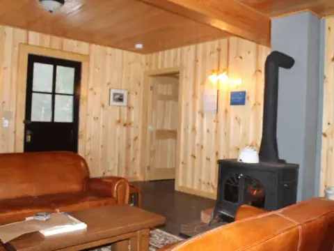 An interior view of a cabin featuring a wood-burning stove and leather furniture.