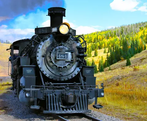 A steam locomotive traveling along a track through a mountainous landscape.