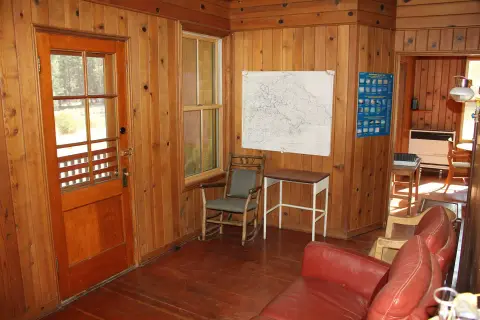 A rustic wooden interior with a door, window, map on the wall, and red armchairs.