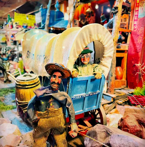 A detailed diorama features handmade figures and a covered wagon.