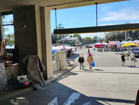People walk through an outdoor street market seen from a shaded structure.