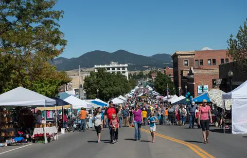 A busy street market with tents and people walking down the middle of the road.