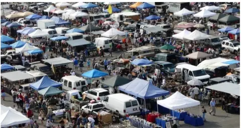 An overhead view of a large outdoor market with many tents, vehicles, and people.