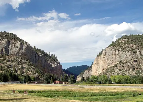 A wide landscape showing a valley between rocky cliffs under a cloudy sky.