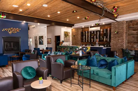 An indoor view of a cozy lounge with armchairs and a bar with wine racks.