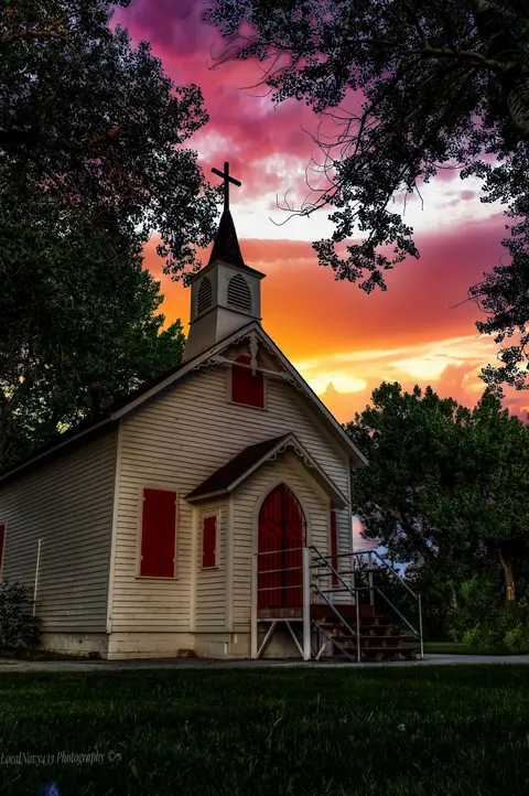 A white church with a steeple stands against a vibrant sunset sky.