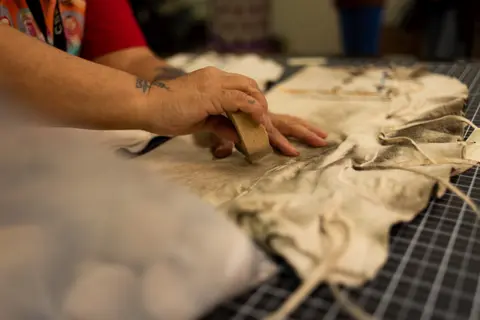 A person uses a small sponge on a piece of hide on a cutting mat.