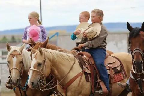 Children ride horses outdoors.