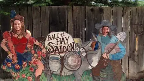 People pose behind a painted wooden photo cutout board depicting saloon characters.