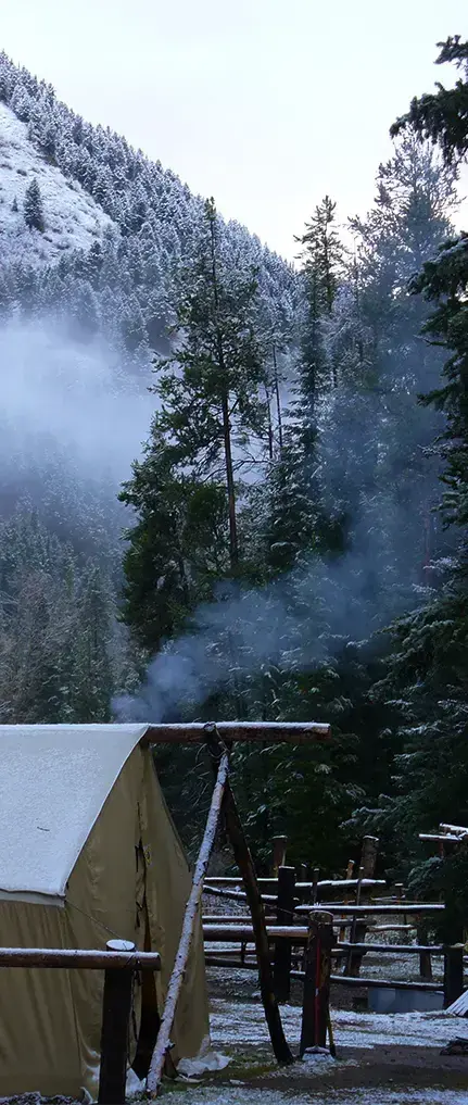 A tent and snowy forest landscape with smoke rising from a chimney.