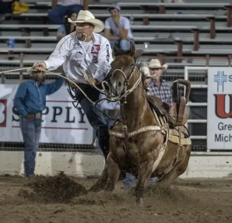 A cowboy ropes a steer from a horse in an arena.