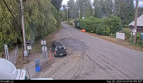 An elevated view of a rural road bordered by trees and a parked vehicle.