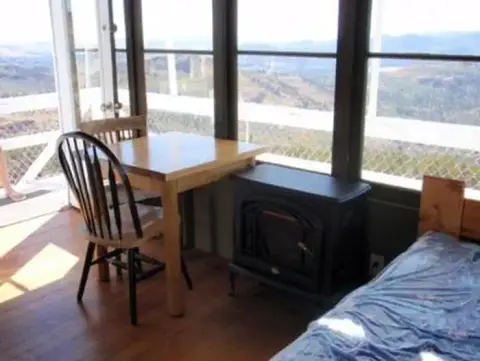 Interior view of a room with a table, chairs, and stove near large windows.