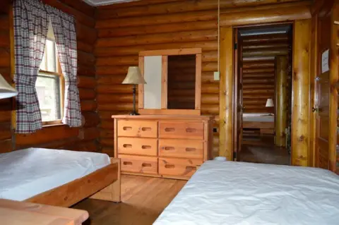 An interior view of a rustic log cabin bedroom with wooden furniture and two beds.
