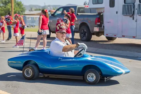 A man wearing a fez drives a small blue car in a parade.