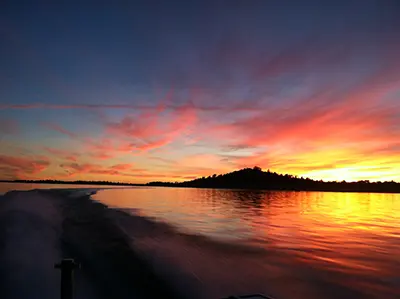 A vibrant sunset over a calm body of water viewed from a moving boat.