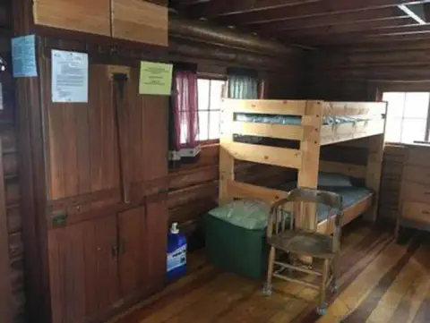 The interior of a rustic cabin featuring a wooden bunk bed, cabinetry, and a chair.