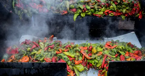 Peppers roasting and smoking on a large outdoor grill.
