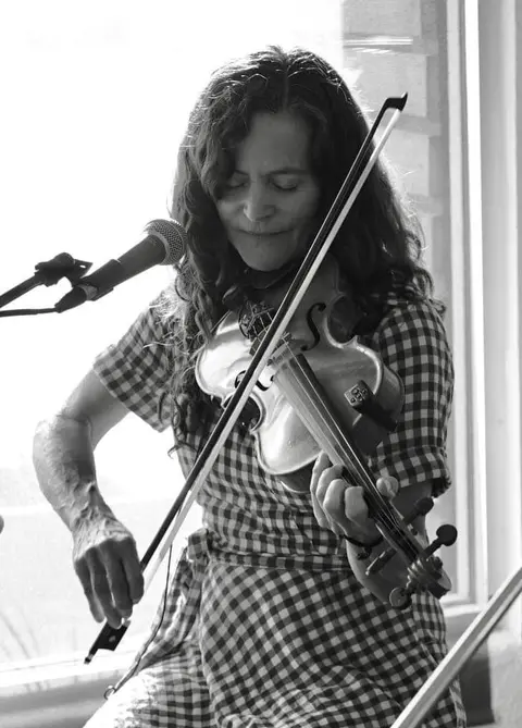 A woman plays a violin in front of a microphone.