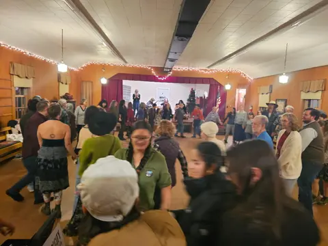 A group of people dancing in a hall with a stage.