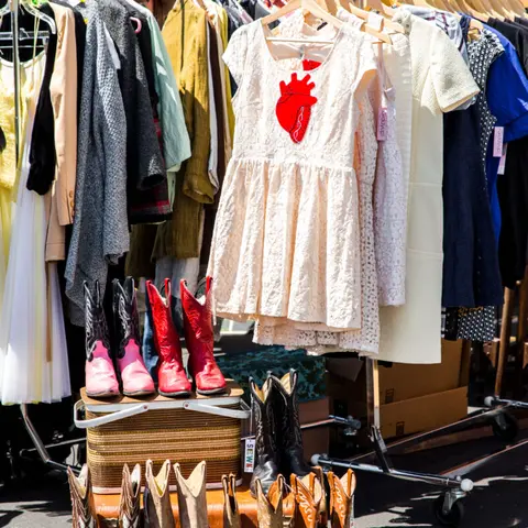 A rack of clothing featuring dresses and cowboy boots displayed on a picnic basket.