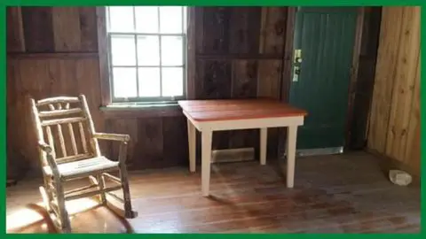 Interior of a rustic room with a wooden rocking chair and a small table near a window.