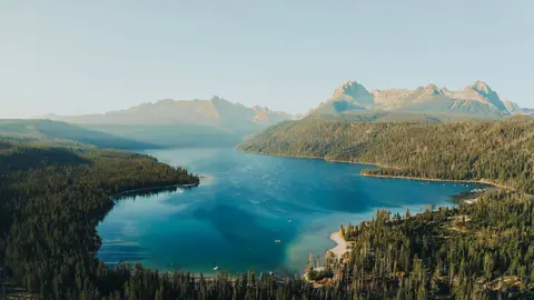 An aerial view of a blue lake surrounded by dense forests and rugged mountains.