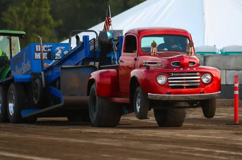 A red vintage Ford truck pulls a sled on a dirt track.