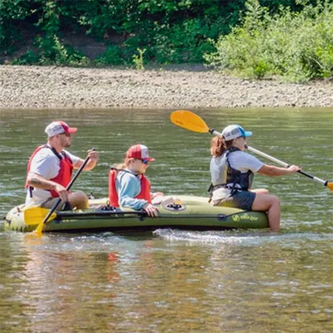 Three people paddling an inflatable boat in a river.