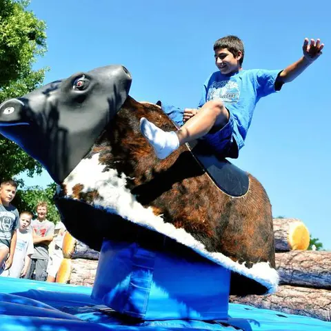 A young boy rides a mechanical bull outdoors.