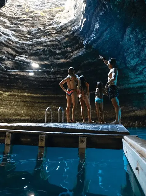 A family stands on a wooden dock inside a cave with a pool of water.