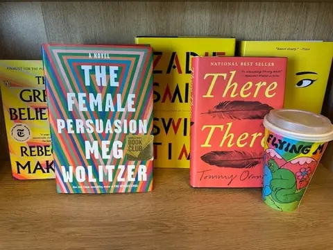 Several books and a patterned coffee cup sit on a wooden shelf.