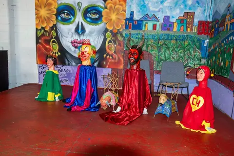 Several colorful puppets and figures are displayed against a painted wall backdrop.