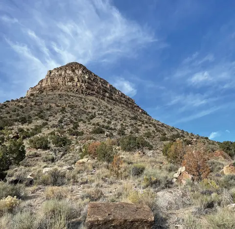 A rugged desert mountain under a blue sky with wispy clouds.