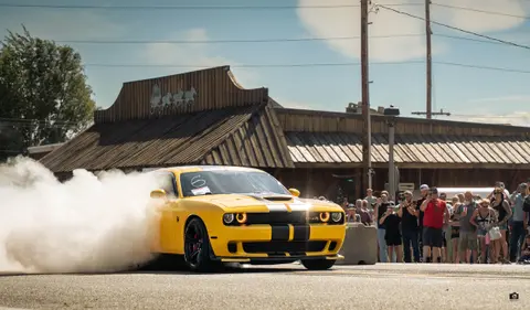 A yellow muscle car burns rubber in front of a crowd of spectators.