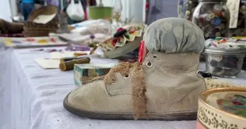 A vintage baby shoe pin cushion sits on a table filled with craft items.