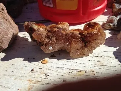 A close-up photograph of a rough mineral specimen on a wooden surface.