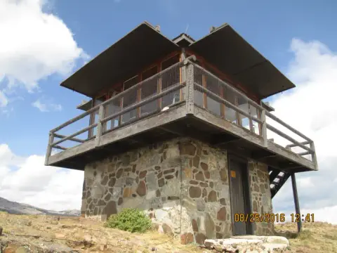A stone and wood fire lookout tower sits on a hill under a partly cloudy sky.