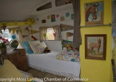 The interior of a small camper features a made bed and colorful wall decorations.