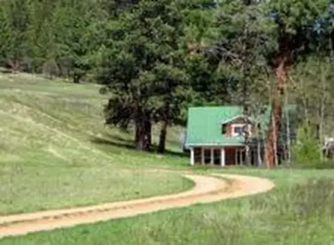 A dirt road curves toward a house surrounded by trees and grassy hills.