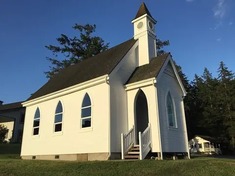 Exterior view of a small white wooden church with a steeple under a blue sky.