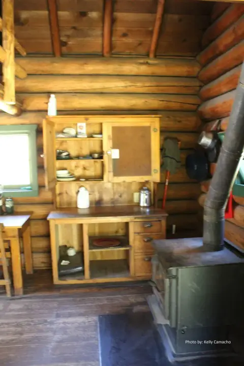 An interior view of a rustic log cabin with a wooden cabinet and wood stove.
