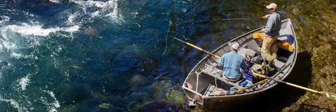 Two people fishing from a boat on a river.