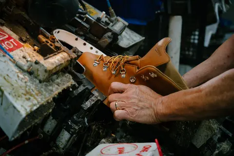 A person works on crafting a leather boot using a machine.