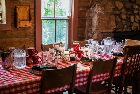 A dining table set with a red and white checkered tablecloth inside a rustic cabin.