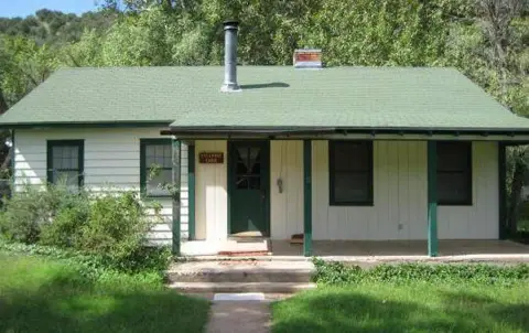 A single-story white cabin with a green roof and a front porch.