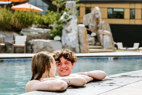 Two people relax in a swimming pool outdoors.